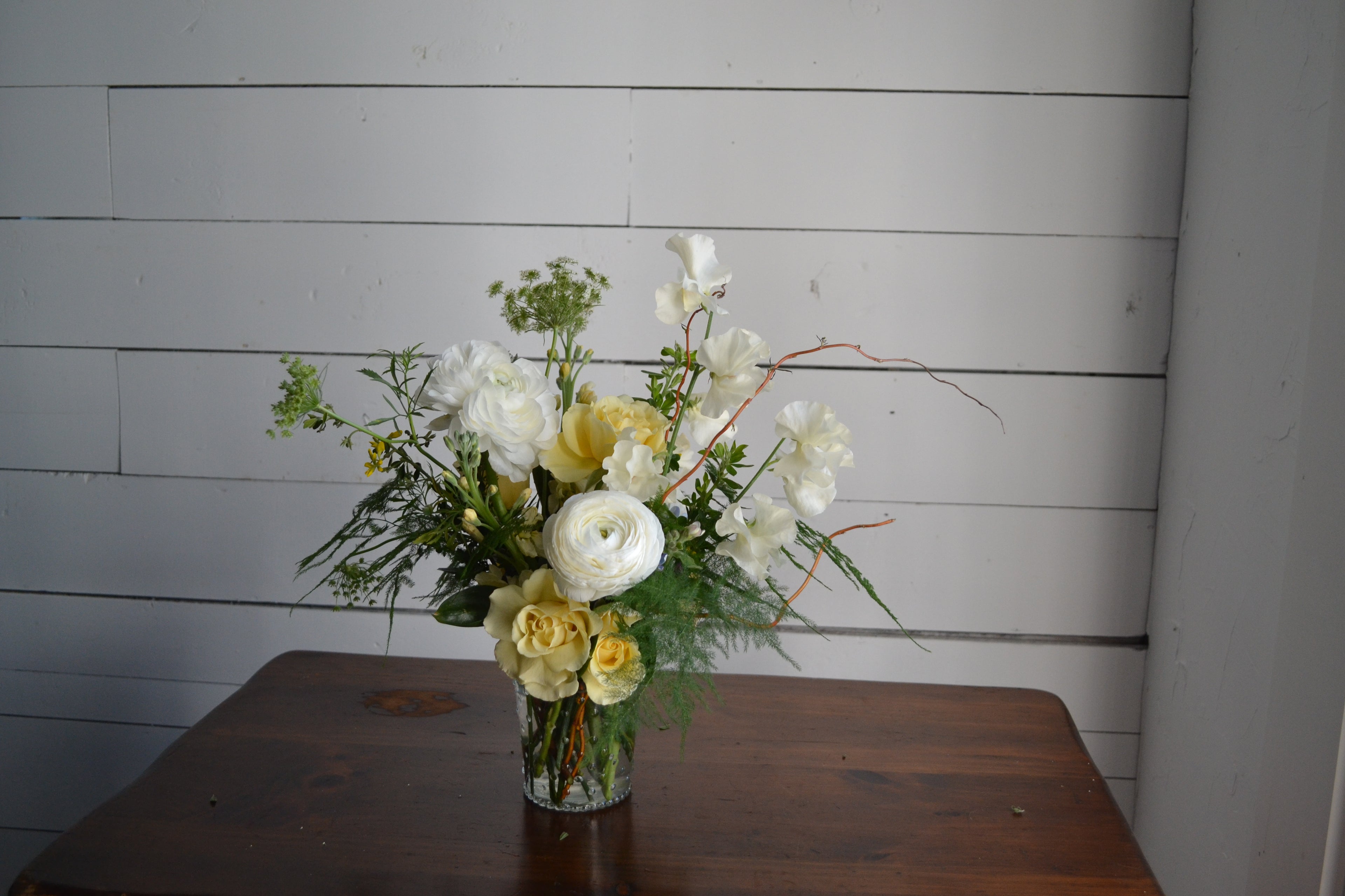 Bouquet of flowers in a vase on a wooden table with a white paneled wall background