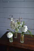 White flowers in clear glass bottles against a wooden background