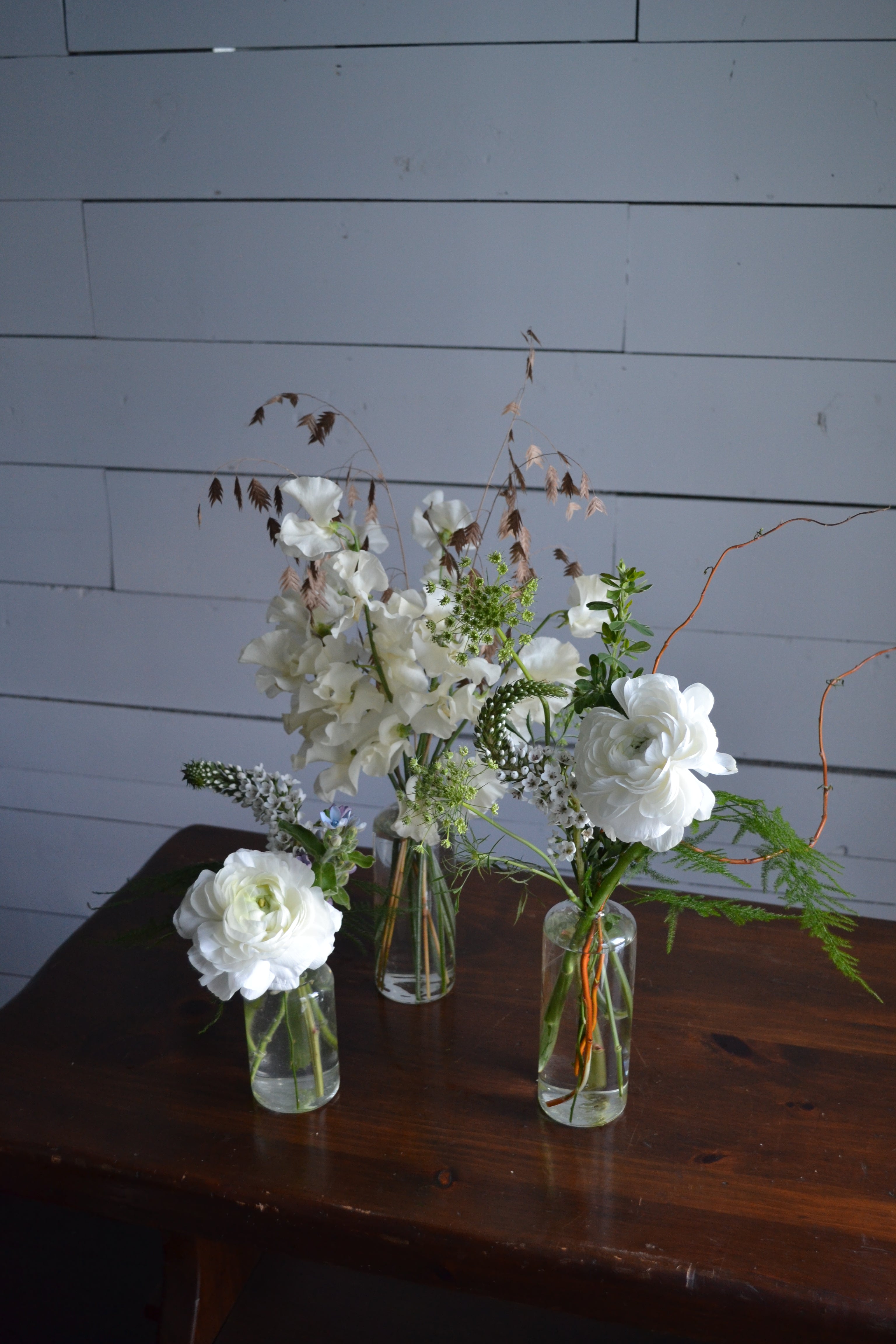 White flowers in clear glass bottles against a wooden background