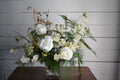 Floral arrangement in a vase on a wooden table with a white paneled background