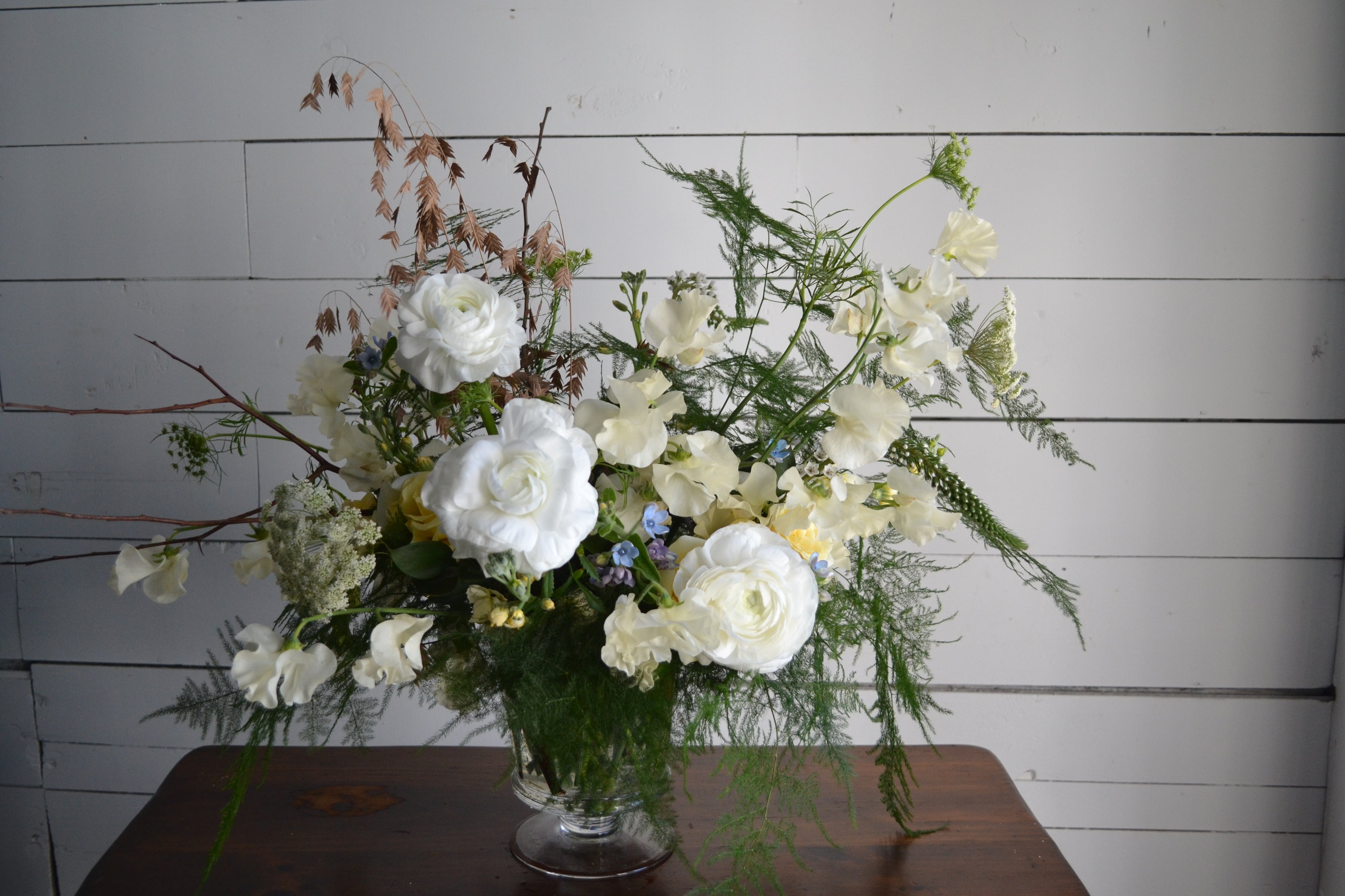 Floral arrangement in a vase on a wooden table with a white paneled background